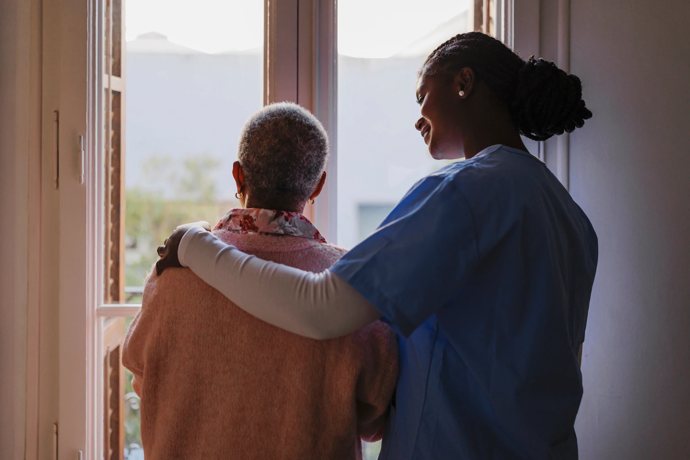 A carer with her arm around an older woman at a window
