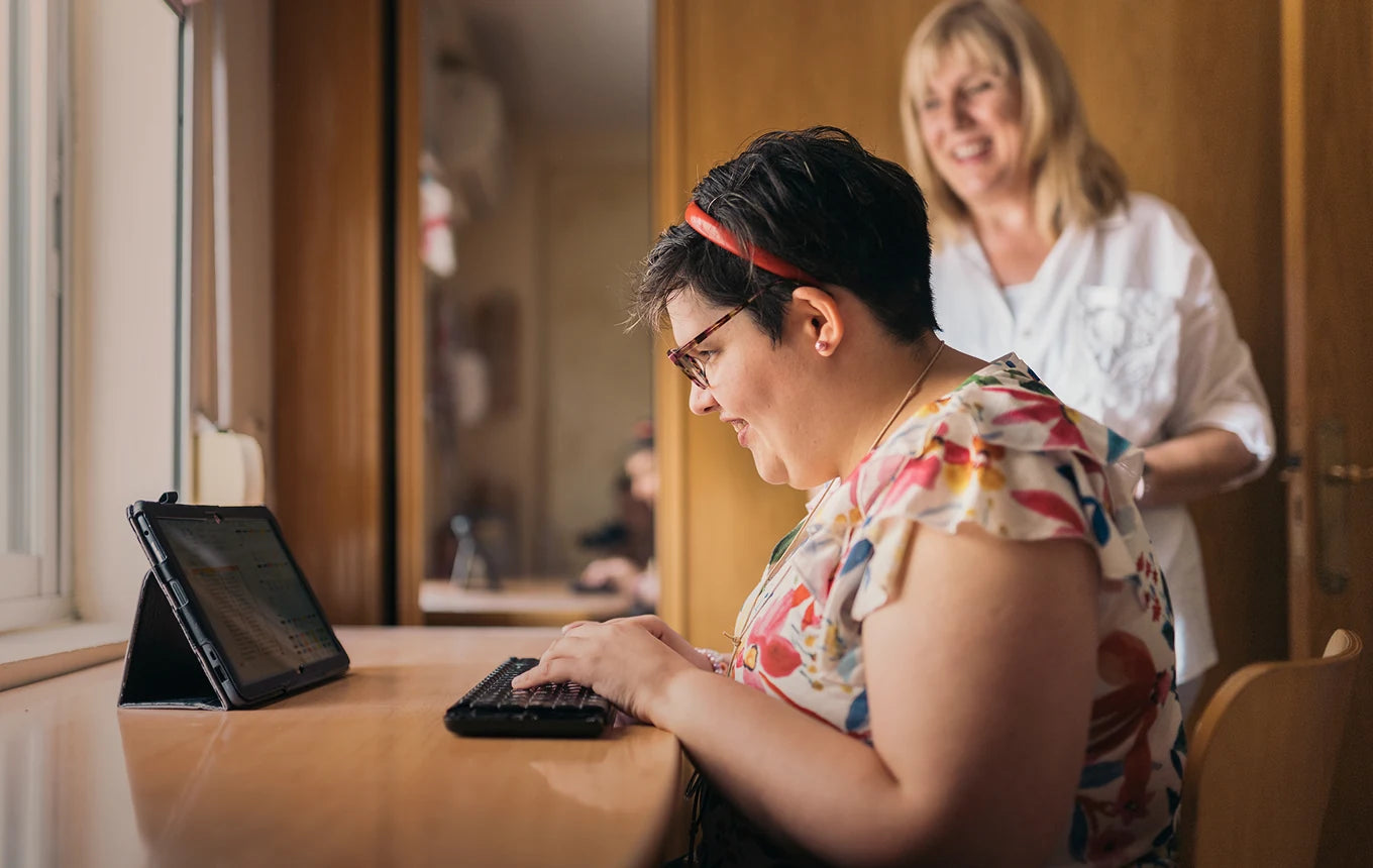 A woman typing at her desk while a support worker looks on